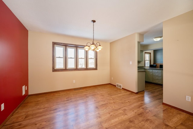 unfurnished dining area featuring a chandelier, visible vents, baseboards, and wood finished floors