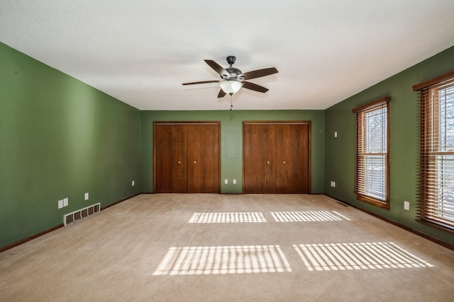 unfurnished bedroom featuring carpet flooring, visible vents, multiple closets, and ceiling fan