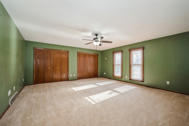 unfurnished bedroom with visible vents, ceiling fan, multiple closets, a textured ceiling, and carpet flooring