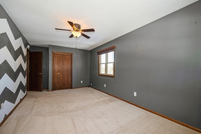 unfurnished bedroom featuring baseboards, light colored carpet, ceiling fan, and a textured ceiling