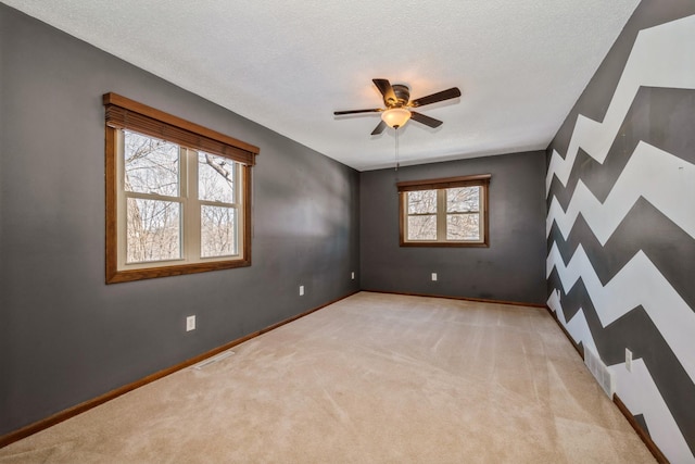 carpeted empty room featuring visible vents, baseboards, a textured ceiling, and ceiling fan