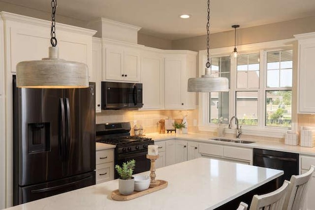 kitchen with a sink, white cabinets, backsplash, black appliances, and decorative light fixtures