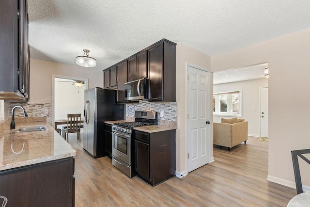 kitchen with dark brown cabinetry, light wood finished floors, light stone countertops, stainless steel appliances, and a sink