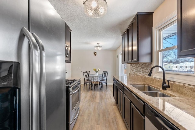 kitchen featuring decorative backsplash, appliances with stainless steel finishes, light wood-style floors, a sink, and dark brown cabinets