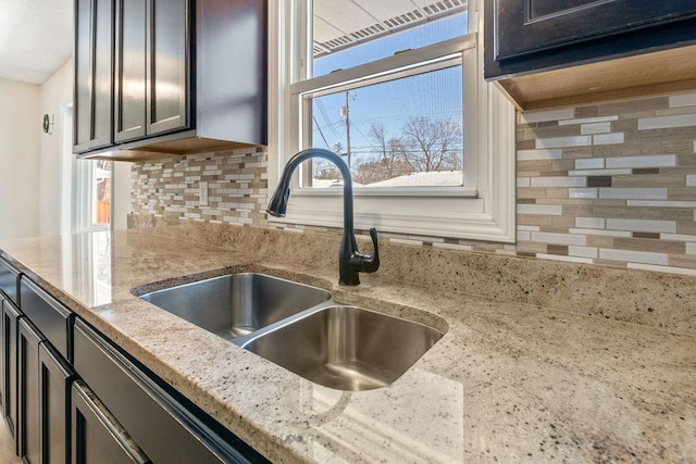 kitchen with light stone counters, backsplash, and a sink