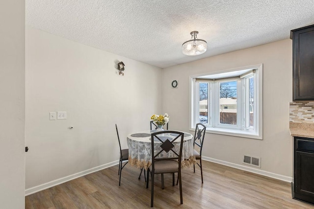 dining space featuring light wood-style floors, visible vents, a textured ceiling, and baseboards