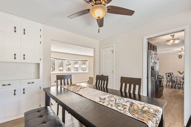 dining room with light wood-style flooring, a ceiling fan, and a textured ceiling