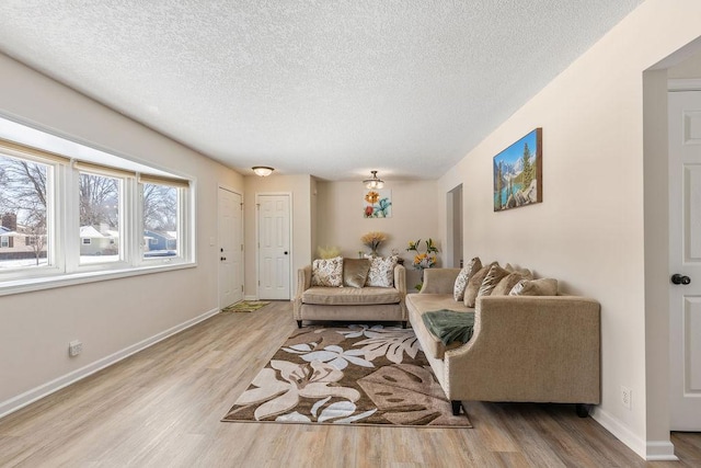 living room with a textured ceiling, light wood-type flooring, and baseboards