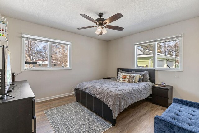 bedroom featuring a ceiling fan, a textured ceiling, baseboards, and wood finished floors