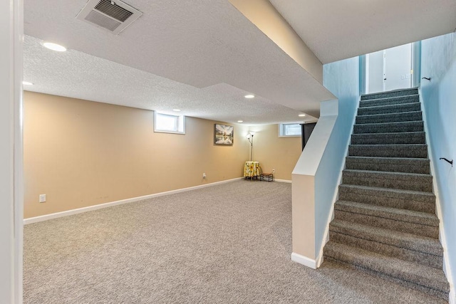 basement with a textured ceiling, carpet floors, visible vents, and baseboards