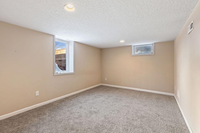 basement featuring a textured ceiling, a healthy amount of sunlight, carpet, and baseboards