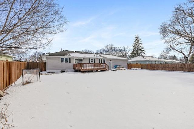 snow covered rear of property with a fenced backyard and a deck