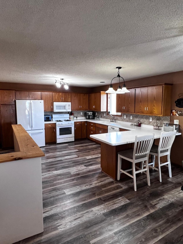 kitchen with dark wood-type flooring, a sink, white appliances, a peninsula, and light countertops