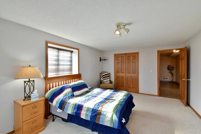 bedroom with visible vents, a textured ceiling, a closet, baseboards, and light colored carpet