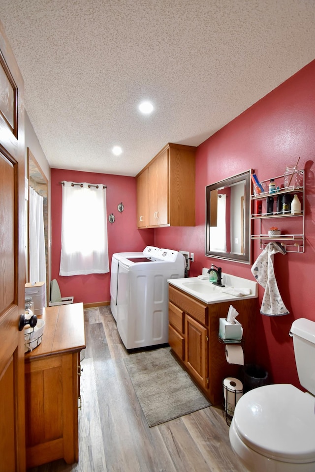 clothes washing area with a sink, washer and dryer, a textured ceiling, light wood finished floors, and laundry area