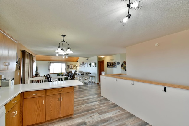 kitchen featuring decorative light fixtures, light countertops, light wood-type flooring, a peninsula, and white dishwasher