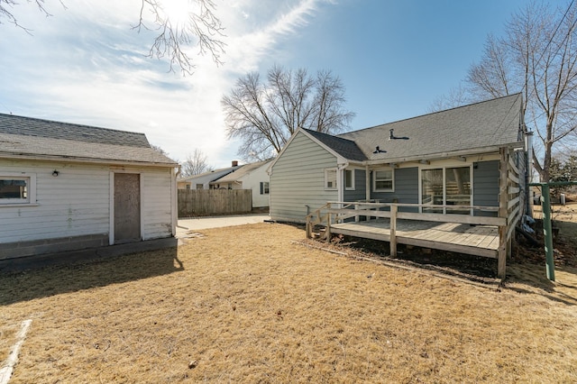 back of house with a shingled roof, a deck, and fence