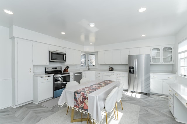 kitchen featuring recessed lighting, stainless steel appliances, white cabinets, light countertops, and glass insert cabinets