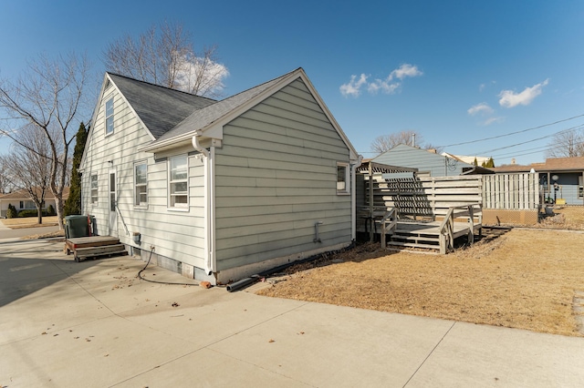 view of side of home with a patio area, a deck, and roof with shingles