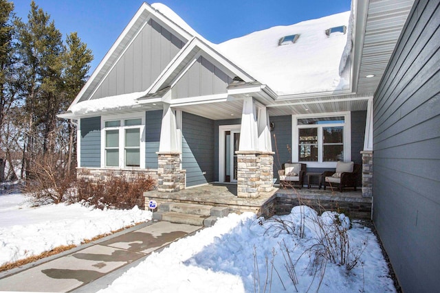 snow covered property entrance featuring covered porch, stone siding, and board and batten siding