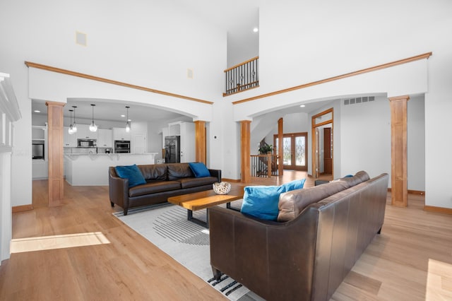 1502 Epperstone Enclave, Byron, MN 55920 - living room featuring decorative columns, light wood-style flooring, arched walkways, and a towering ceiling
