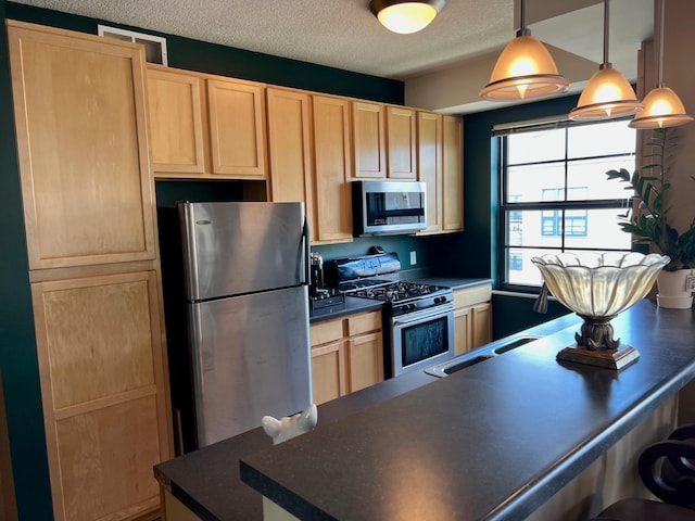 kitchen featuring a textured ceiling, a breakfast bar area, stainless steel appliances, light brown cabinetry, and dark countertops