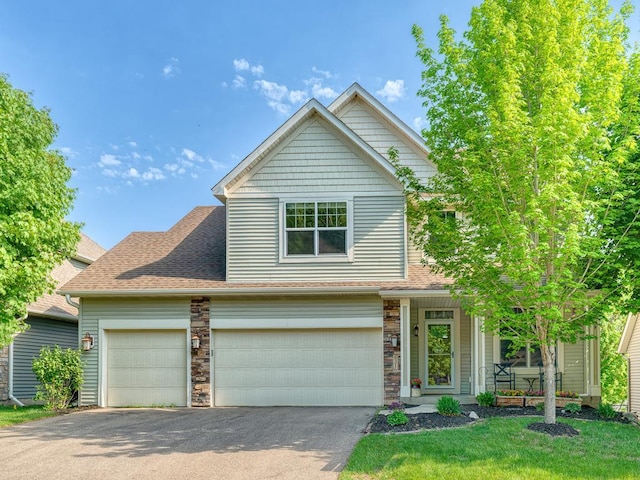 view of front of home with driveway, roof with shingles, a front lawn, an attached garage, and a porch