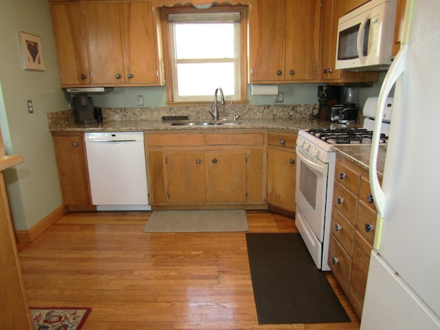 kitchen with baseboards, white appliances, a sink, and light wood-style floors