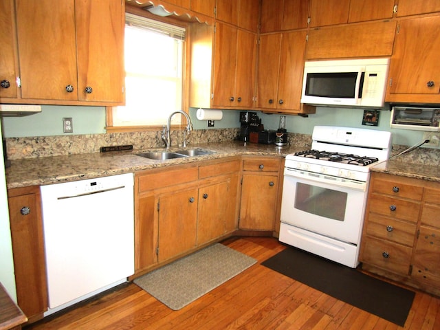 kitchen with white appliances, brown cabinets, a sink, and wood finished floors