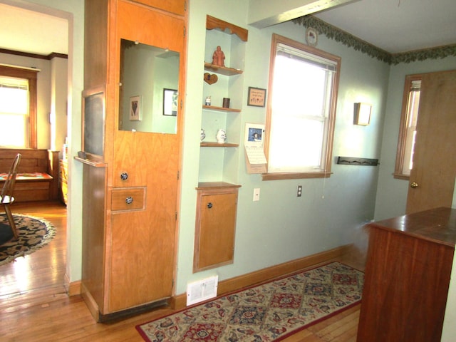 corridor with built in shelves, light wood finished floors, visible vents, and baseboards