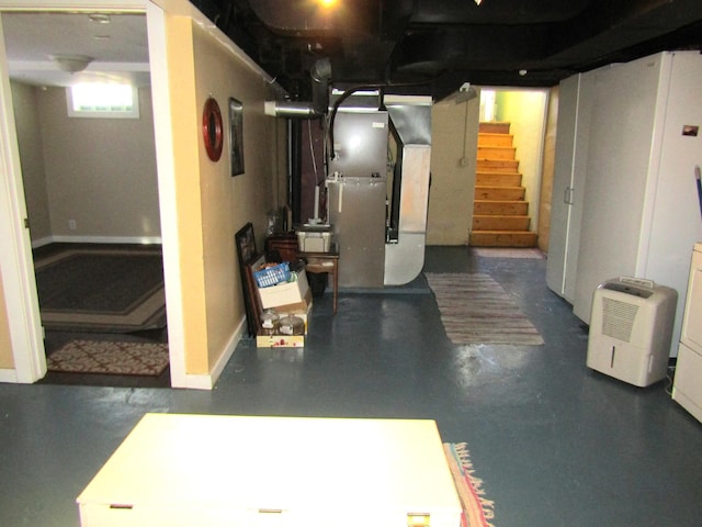 basement featuring baseboards, heating unit, and stairs