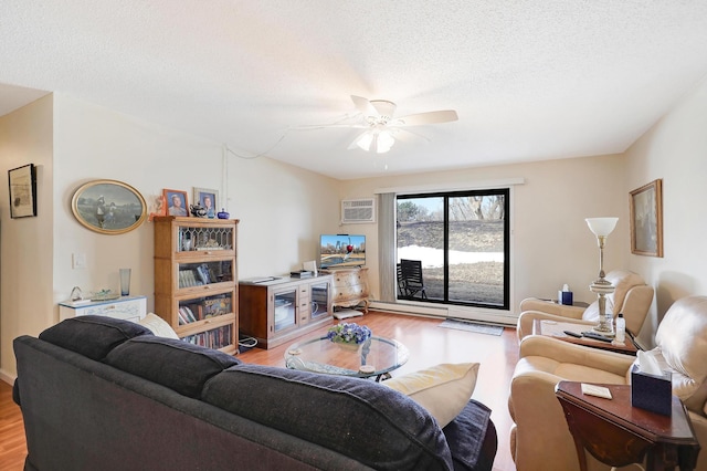 living room featuring light wood finished floors, an AC wall unit, a textured ceiling, and ceiling fan