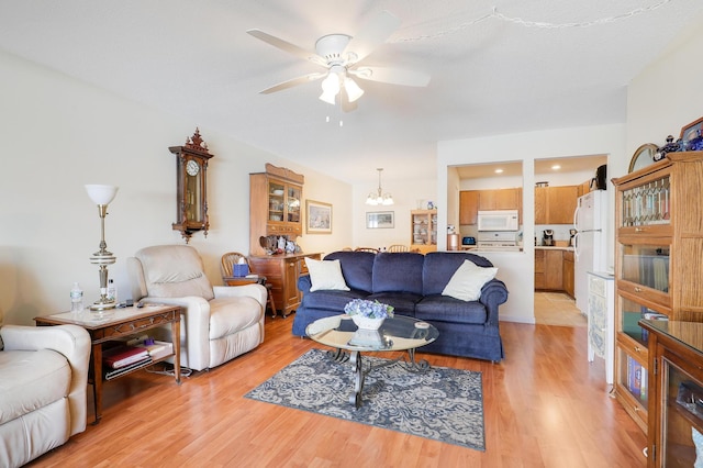 living area with ceiling fan with notable chandelier and light wood finished floors