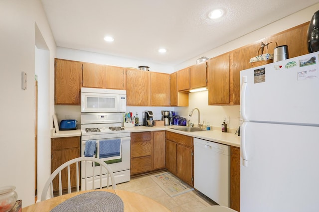 kitchen featuring white appliances, brown cabinetry, recessed lighting, a sink, and light countertops