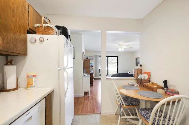 kitchen with white appliances, light tile patterned floors, brown cabinetry, ceiling fan, and light countertops