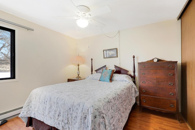 bedroom with a ceiling fan, wood finished floors, and baseboard heating