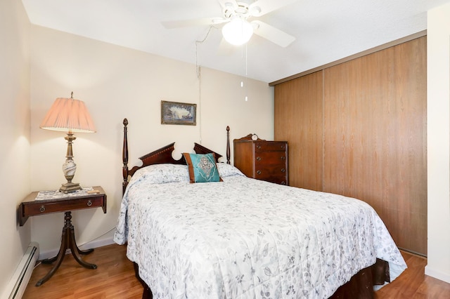 bedroom with ceiling fan, a baseboard heating unit, baseboards, and wood finished floors