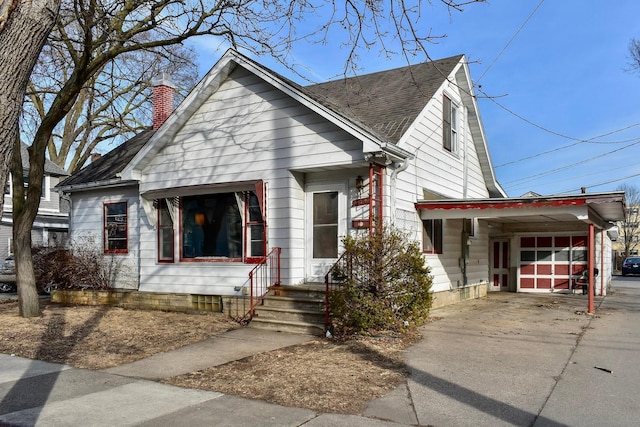 view of front facade with concrete driveway, an attached carport, a chimney, and a shingled roof