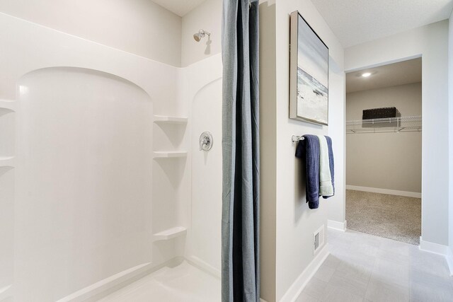 bathroom featuring visible vents, a shower stall, a walk in closet, and baseboards