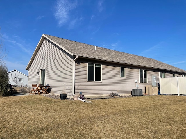 rear view of property with a yard, cooling unit, and a shingled roof