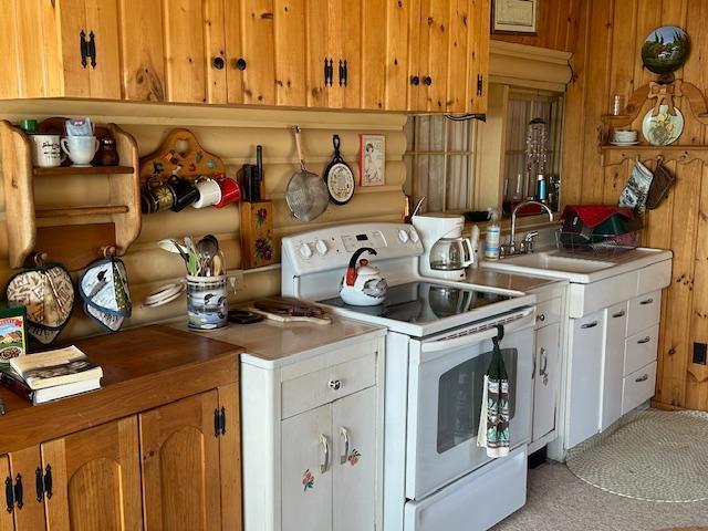 kitchen with rustic walls, brown cabinets, light countertops, white electric range, and a sink