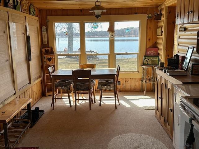 dining area with a water view, rustic walls, wood walls, and light colored carpet