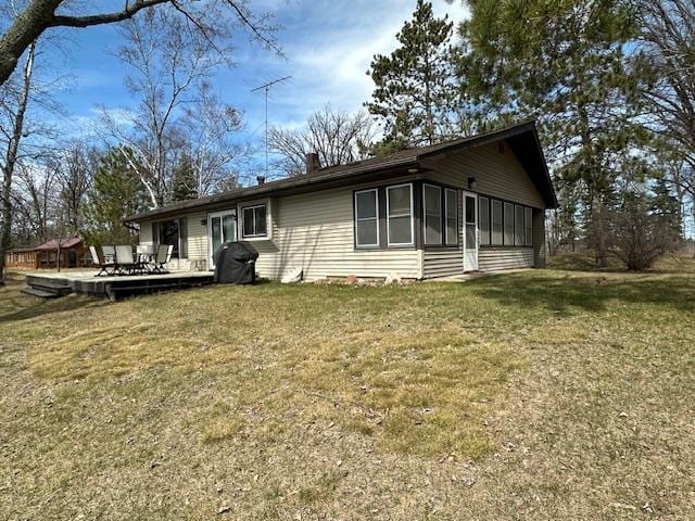 view of side of property with a yard, a chimney, a sunroom, and a wooden deck