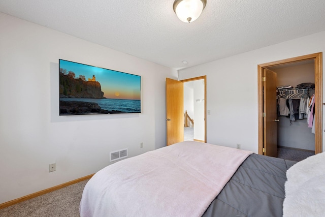 carpeted bedroom featuring a walk in closet, baseboards, visible vents, and a textured ceiling