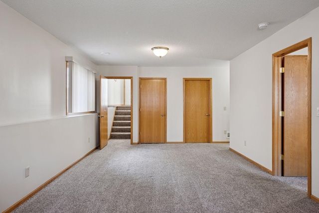 unfurnished bedroom featuring baseboards, carpet floors, two closets, and a textured ceiling