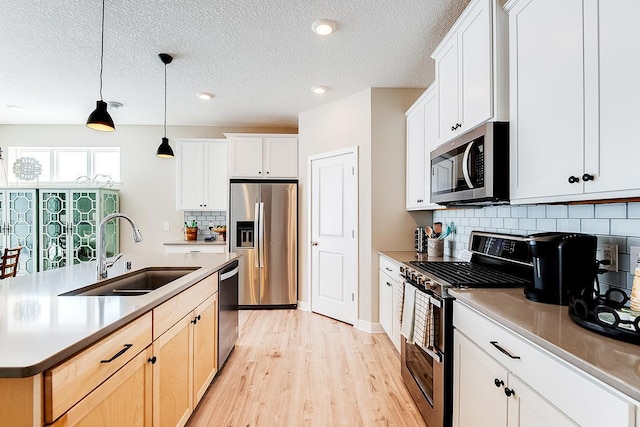 kitchen with an island with sink, appliances with stainless steel finishes, decorative light fixtures, light wood-style floors, and a sink