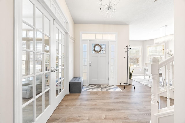 foyer entrance with a textured ceiling, wood finished floors, a wealth of natural light, and a chandelier