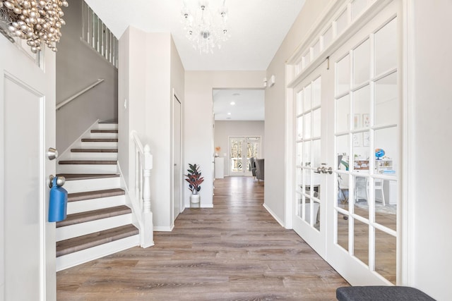 foyer featuring stairway, wood finished floors, baseboards, french doors, and a chandelier