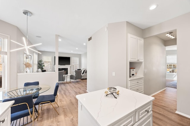 kitchen with white cabinetry, recessed lighting, light wood-style floors, a fireplace, and light stone countertops