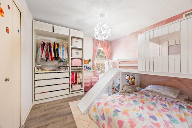 bedroom with a closet, a textured ceiling, an inviting chandelier, and wood finished floors